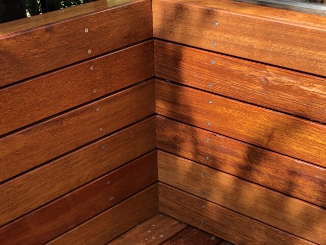 Built-in hardwood outdoor bench corner on deck, slatted boards with stainless fixings.