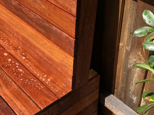 Detail of hardwood slatted bench on deck, water droplets near fence.