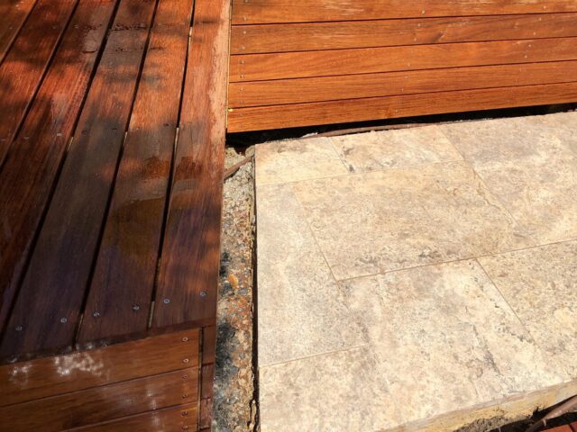 Outdoor hardwood deck with integrated corner bench beside stone paving.