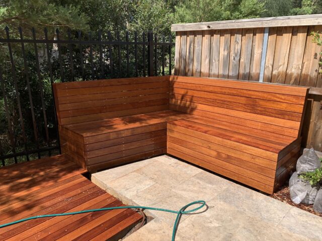 Built-in L-shaped timber bench on patio, adjacent to deck and fenced garden.