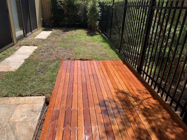 New timber deck beside black fence, with lawn and stepping stones.