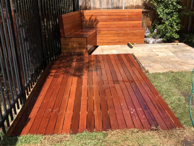 Wet timber deck with built-in corner bench beside metal and timber fences.