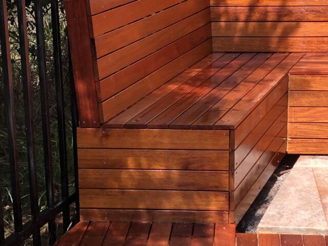 Timber decking with integrated corner bench seat beside black metal fence.