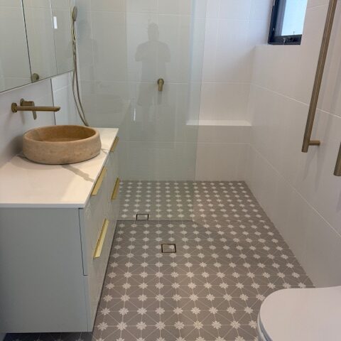Modern bathroom with walk-in shower, star-patterned tiles, brass fixtures and grab rail, floating vanity with stone vessel basin.