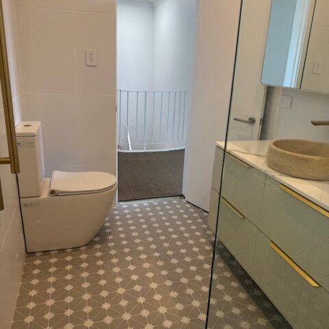 Renovated bathroom with patterned floor tiles, floating vanity, stone basin, glass shower, and toilet.