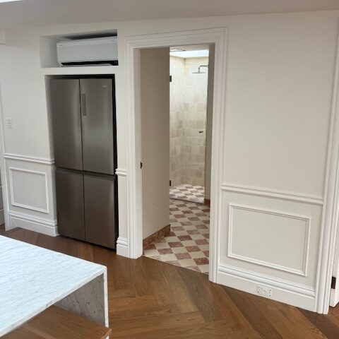 Kitchen renovation with marble island, herringbone timber floor, stainless fridge, doorway to checkerboard-tiled bathroom.