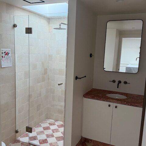Renovated bathroom with skylit glass shower, checkerboard floor, and stone vanity.