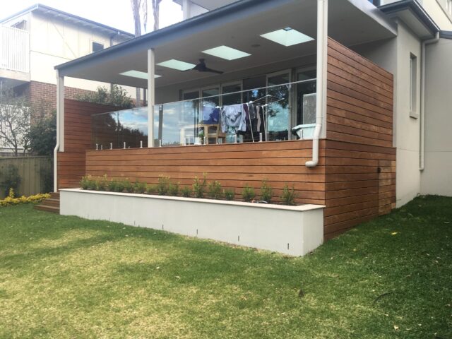 Modern covered deck with timber cladding, glass balustrade, skylights, and raised planter.