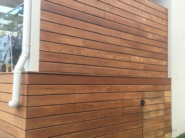 Horizontal timber slat privacy screen with enclosed base and access door beside lawn.