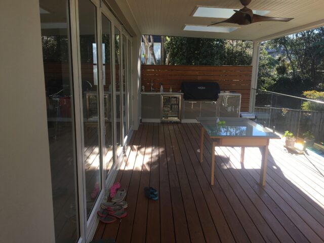Covered timber deck with skylights, ceiling fan, outdoor kitchen and glass balustrade.