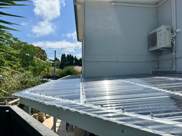 Transparent corrugated polycarbonate pergola roof over patio, attached to house exterior.