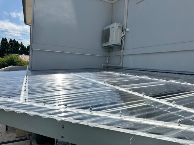 Translucent corrugated polycarbonate patio roof attached to rendered house wall.