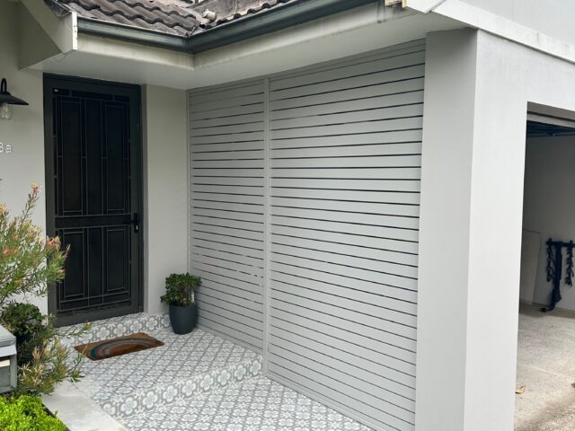Updated front porch with grey slatted screen, patterned tiles, and metal door.