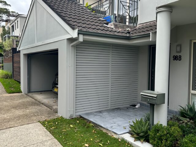 Two-storey home facade with slatted garage screen, tiled porch, and tidy landscaping.