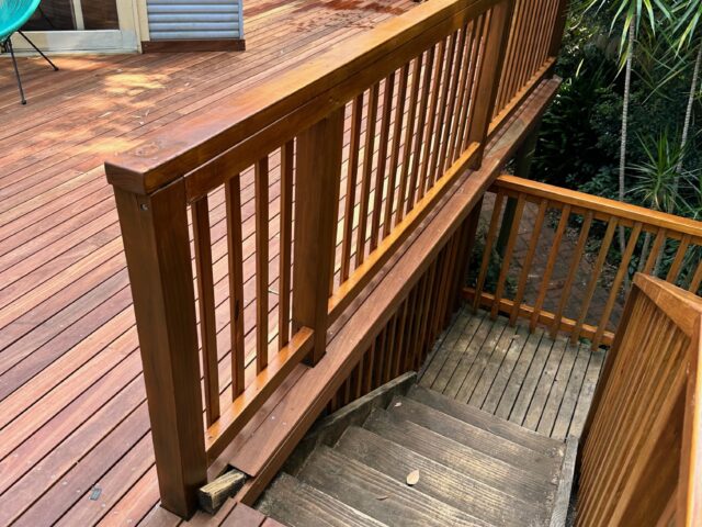Timber deck with balustrade and stairs descending to leafy garden beside house.