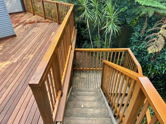 Timber deck with balustrades and stairs descending to garden amid lush plants.