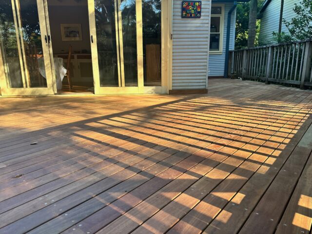 Afternoon sun casts lattice shadows across hardwood deck with sliding doors and railing.