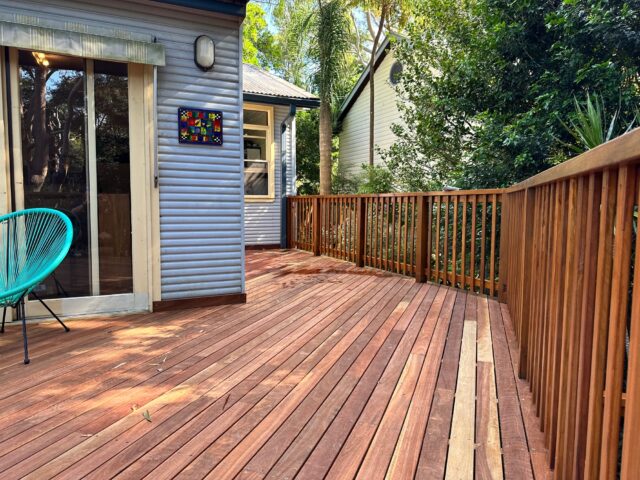 Spacious hardwood deck with slatted balustrade, sliding door and turquoise outdoor chair, leafy surrounds.