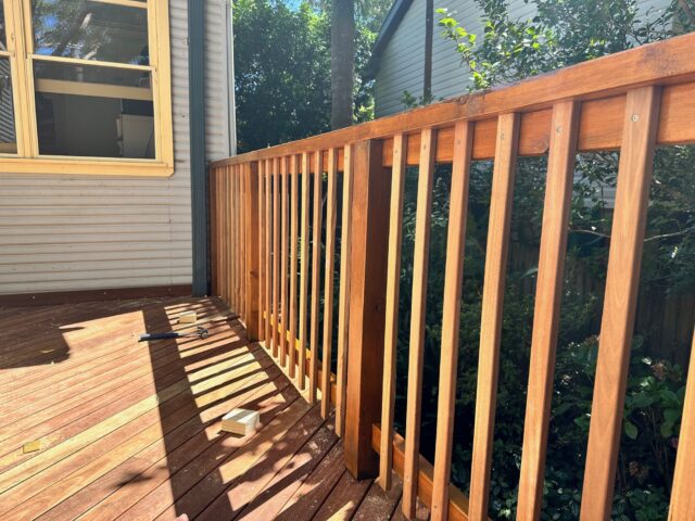 Timber deck with vertical balustrade beside weatherboard house, hand tools on sunlit boards.