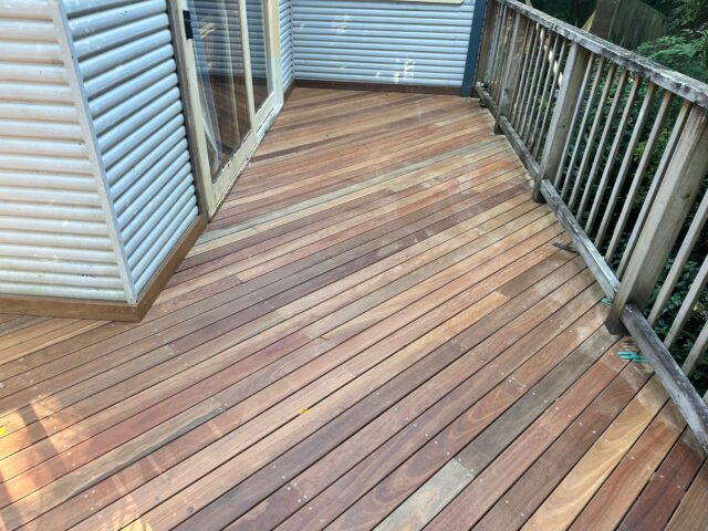 Hardwood deck with angled boards, timber balustrade and sliding doors beside corrugated cladding.