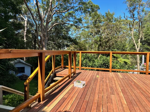 Timber deck with handrail and stairs, overlooking a leafy backyard and tall trees.
