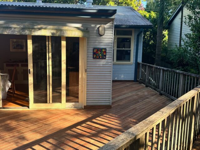 Elevated timber deck with balustrade and sliding doors, surrounded by garden trees.