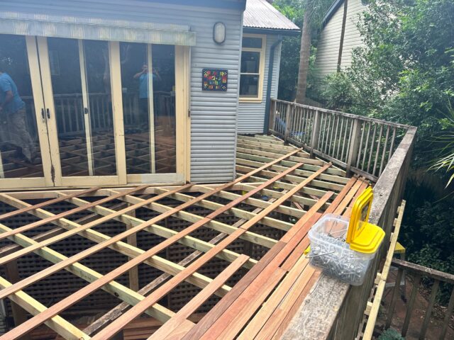 Timber deck rebuild at sliding doors; joists exposed, partial boards laid, screws nearby.