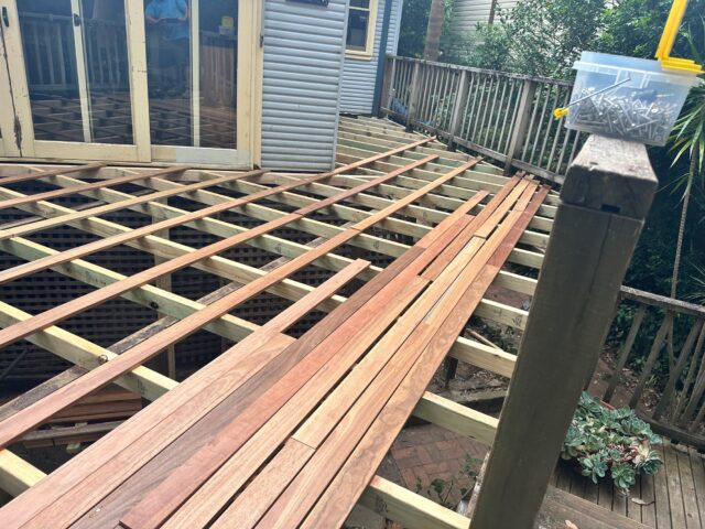 Hardwood decking boards laid across timber joists; box of screws on balustrade.