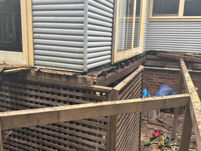 Decking removed beneath sliding door; exposed joists, lattice screening, tools scattered on ground.