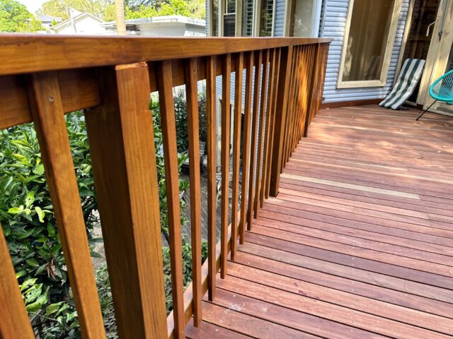 Hardwood decking with vertical timber balustrade beside house, facing a leafy backyard.