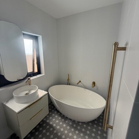 Modern renovated bathroom with freestanding tub, vessel sink, brass tapware, and patterned tile floor.