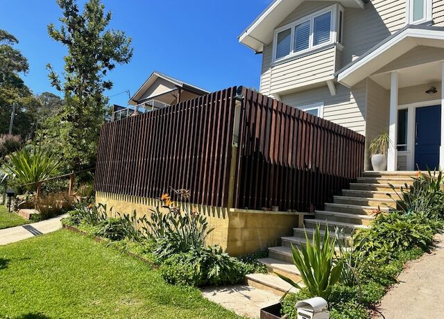 Vertical timber batten screen around raised deck, landscaped steps to modern home.