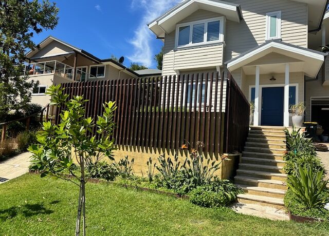 Two-storey weatherboard house with timber slat privacy screen, raised terrace and landscaped steps.