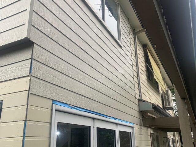 Two-storey home with new weatherboard cladding, sliding doors, and deck during renovation.