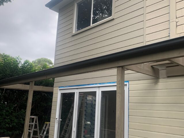 Two-storey weatherboard home with new white-framed sliding doors, deck and pergola under construction.