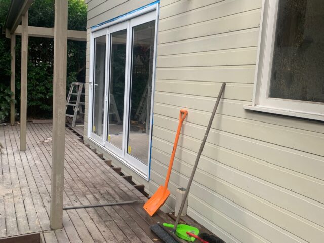 Timber deck and pergola framing during renovation, new sliding doors taped, tools scattered.