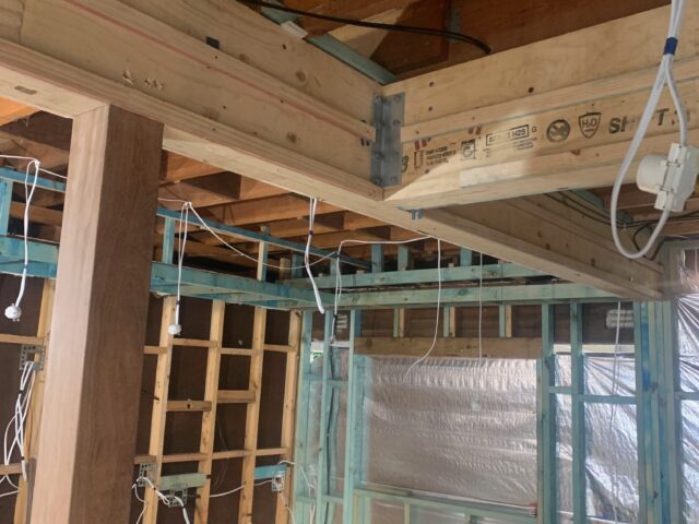 LVL beam bolted to post with metal brackets; exposed framing, wiring and foil insulation.