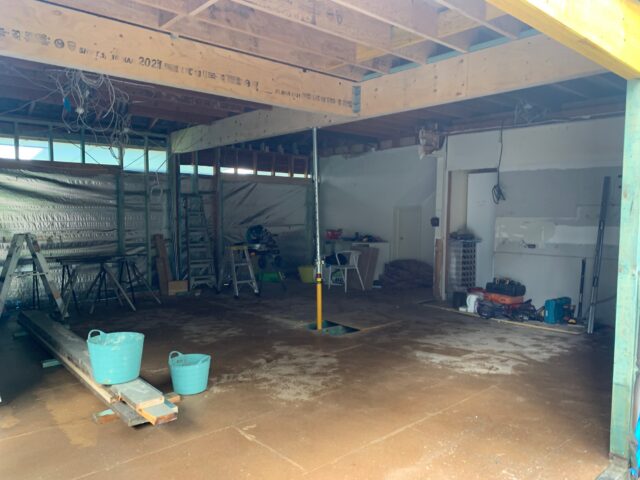 Renovation site with exposed timber framing, ladders, miter saw and tools across unfinished floor.