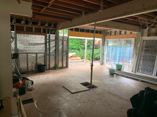 Home extension under construction with exposed framing, support post, and wide opening to garden.