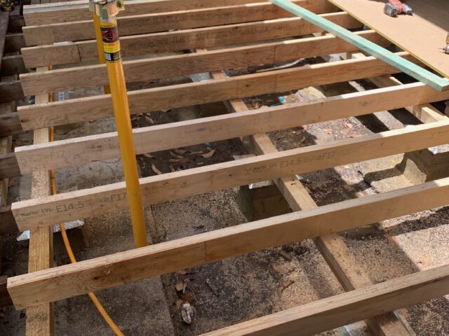 Builder installing new deck joists and flooring sheets; adjustable prop supports frame.