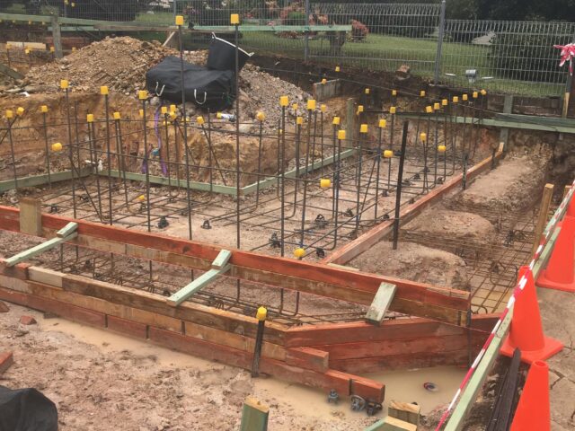 Foundation trench with timber formwork, rebar and safety caps for home extension.