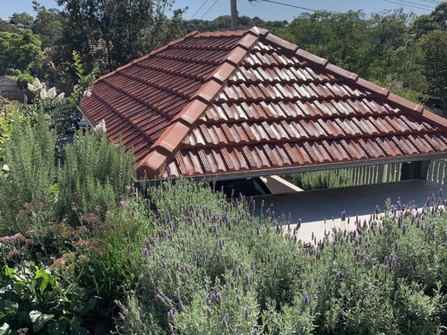 Terracotta tiled hip roof shelter over patio, framed by lavender and shrubs.