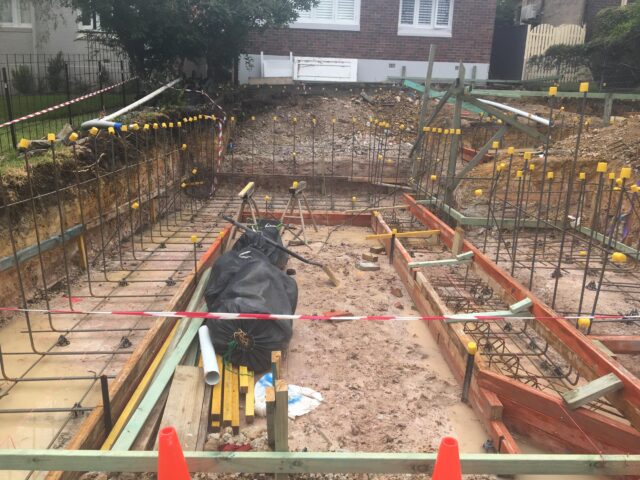Residential footing excavation with capped rebar, timber formwork and warning tape.