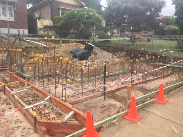 Residential site with footing trenches, rebar cages and formwork for extension foundation.