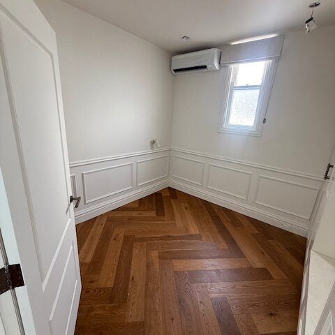 Renovated small room with herringbone timber flooring, white wainscoting, window and split-system AC.