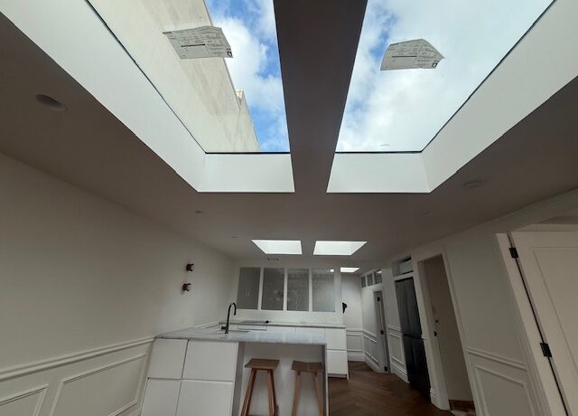 Light-filled renovated kitchen with multiple skylights, white island, stools, herringbone timber flooring.