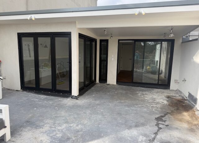 Covered patio extension with black-framed bifold doors and sliding door, concrete base awaiting decking.