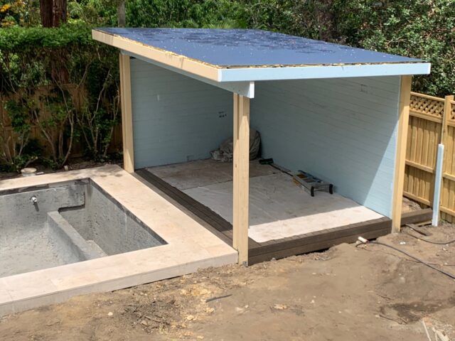 Timber cabana with skillion roof under construction beside concrete pool shell.