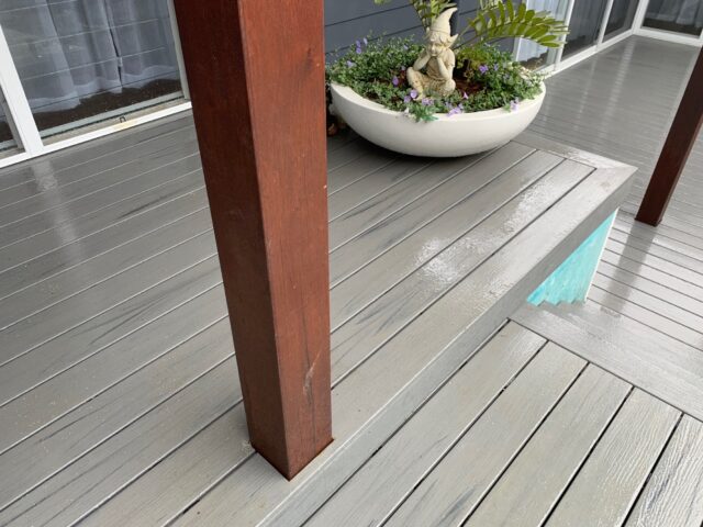 Wet grey timber deck with step detail, hardwood pergola post, and large planter near sliding doors.
