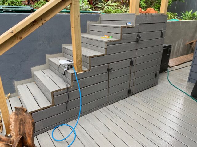 Composite decking stairs with integrated storage doors and timber posts beside a concrete retaining wall.